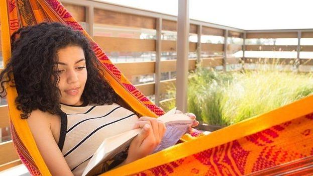 Student reading a book in a hammock on campus